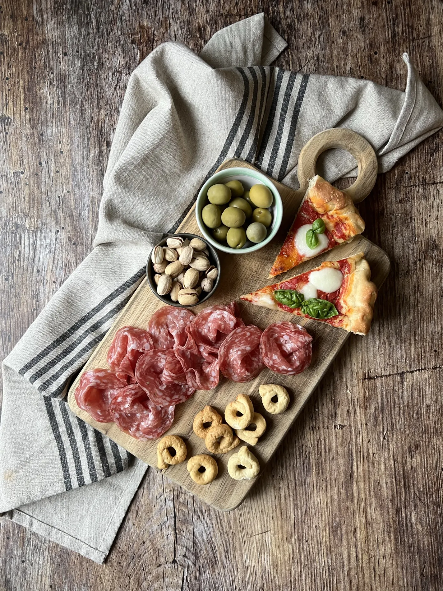 La foto zenitale di un tagliere di salumi, formaggi, taralli e olive
